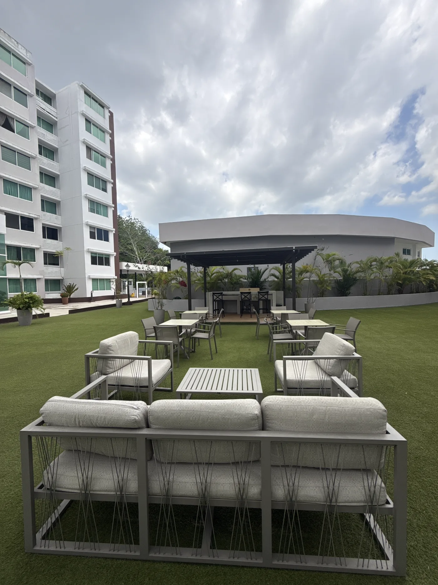 Lounge y área BBQ real, con césped, pérgola y vista al edificio