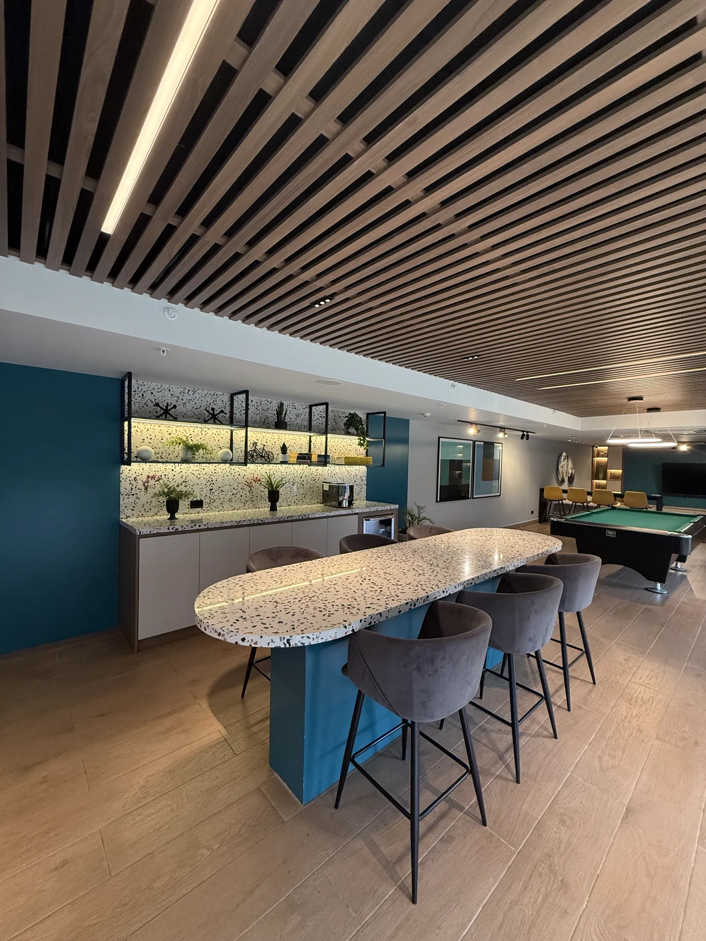 Lounge interior con barra de terrazo, sillas altas y mesa de billar al fondo