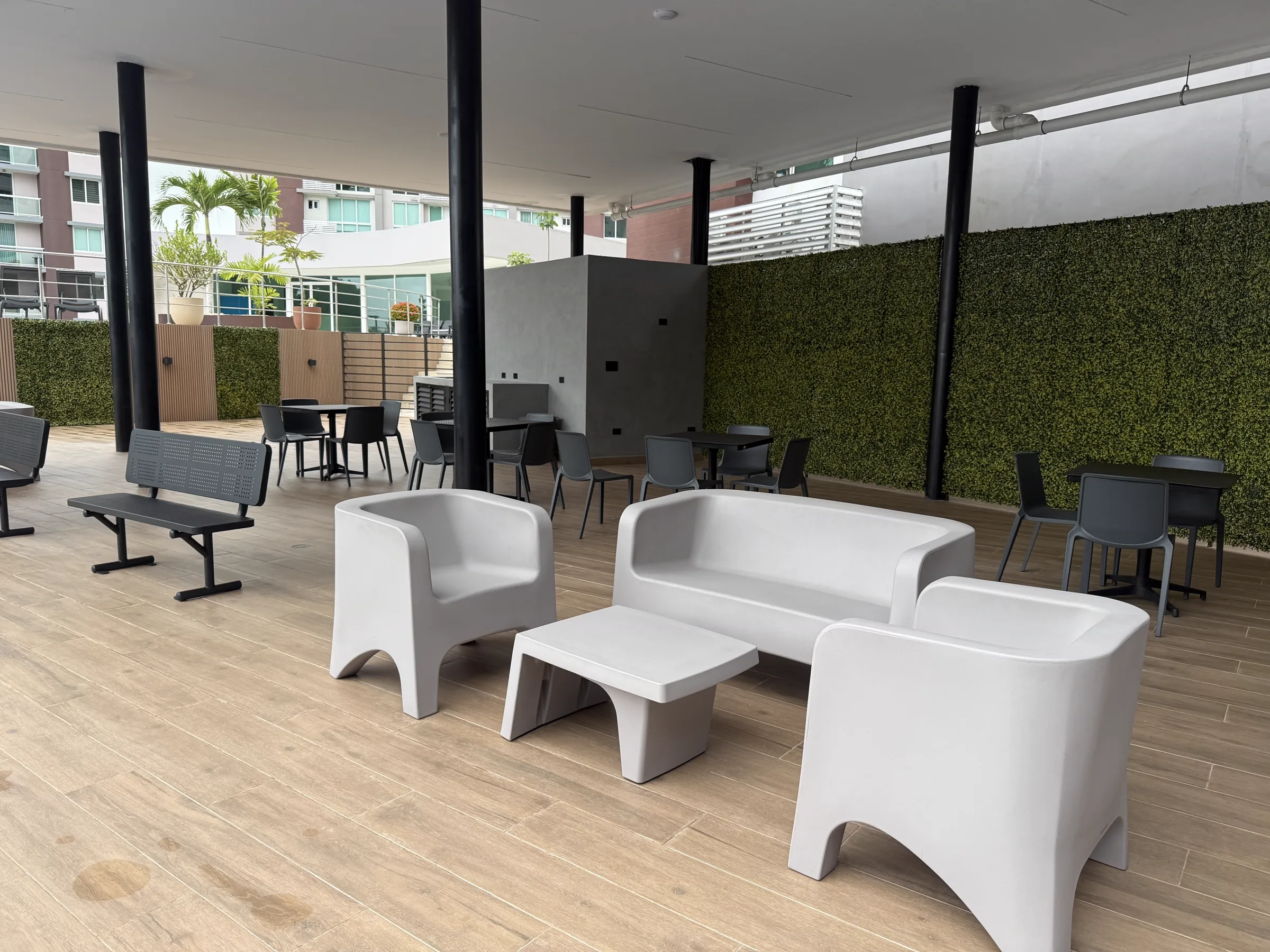 Área de lounge techada con sofás y sillones blancos, mesas y muro verde